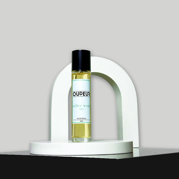 A bottle of perfume with a label that reads 'DUDE', placed on a white, curved pedestal against a grey background.