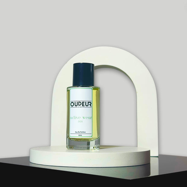 A bottle of perfume with a label that reads 'DUDE', placed on a white, curved pedestal against a grey background.