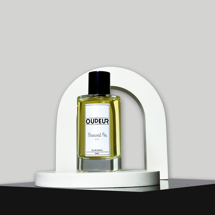 A bottle of perfume with a black cap and a white label, presented on a white stand with a curved design. The brand name 'OUDER' is visible on the label.