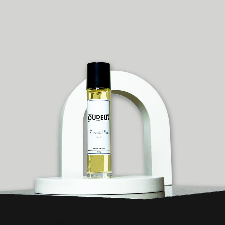 A bottle of perfume with a black cap and a white label, presented on a white stand with a curved design. The brand name 'OUDER' is visible on the label.