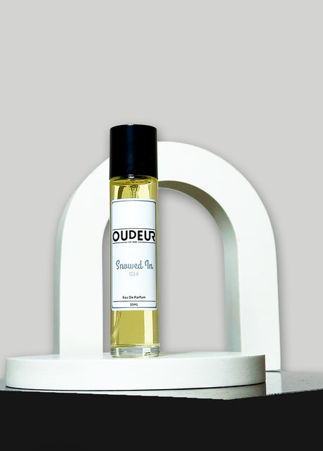 A bottle of perfume with a black cap and a white label, presented on a white stand with a curved design. The brand name 'OUDER' is visible on the label.