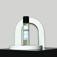 A bottle of Oudeis cologne displayed within a white, curved structure on a grey background.