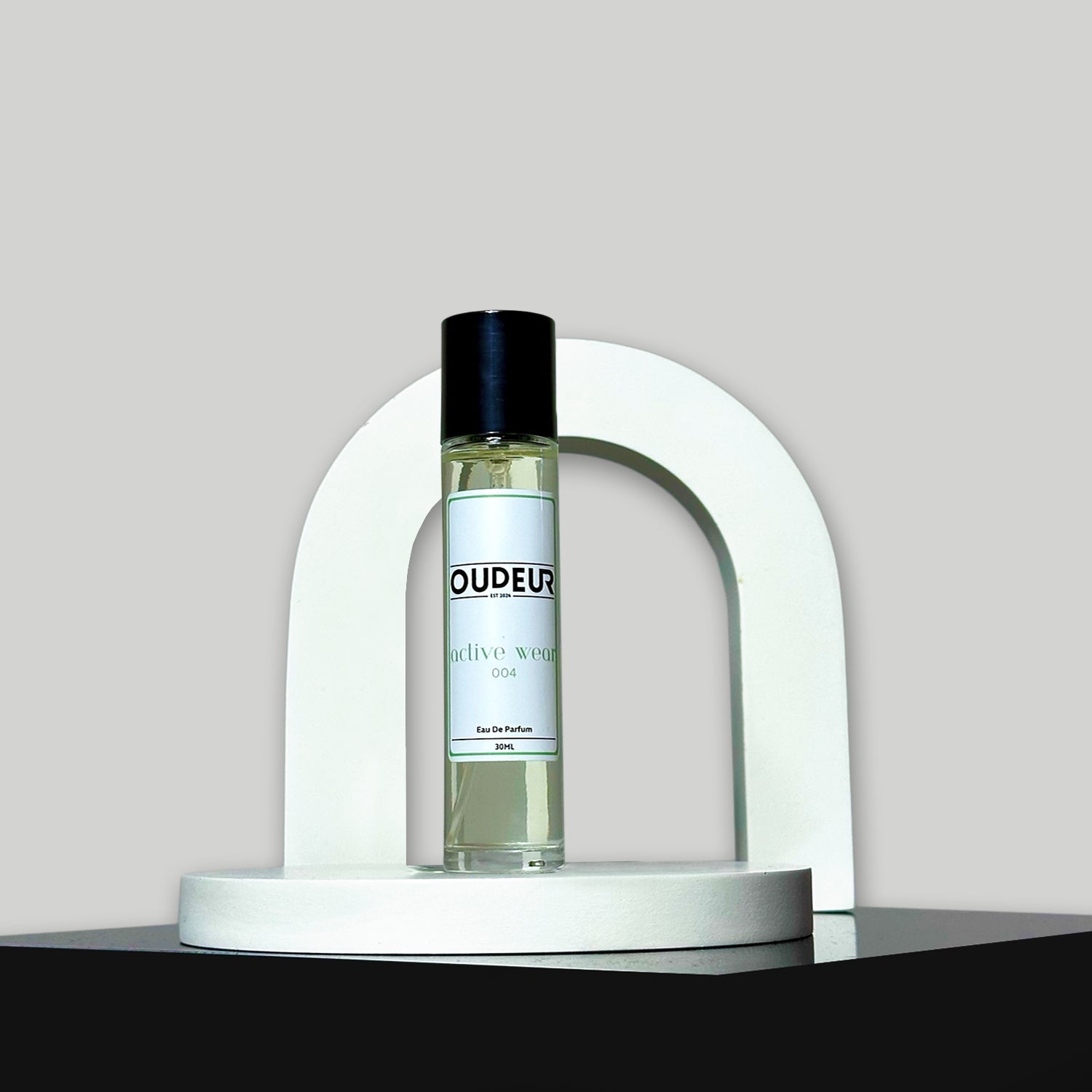 A bottle of Oudeis cologne displayed within a white, curved structure on a grey background.