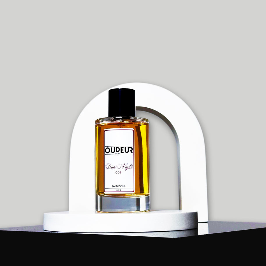 A bottle of perfume with a vibrant red label, displayed in front of a white arch-shaped stand against a grey background.