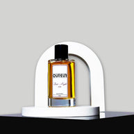 A bottle of perfume with a vibrant red label, displayed in front of a white arch-shaped stand against a grey background.