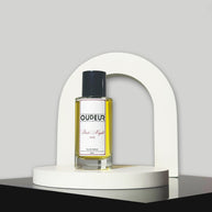 A bottle of perfume with a vibrant red label, displayed in front of a white arch-shaped stand against a grey background.