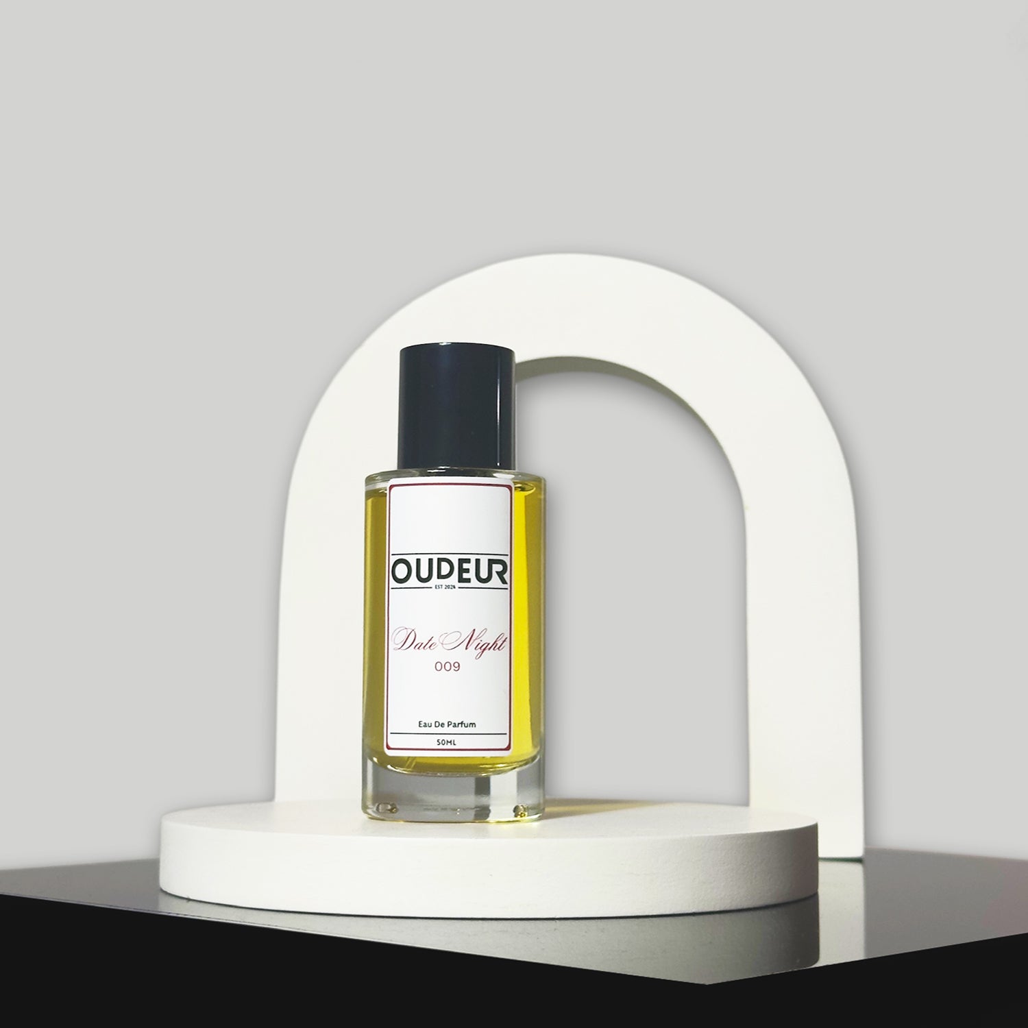 A bottle of perfume with a vibrant red label, displayed in front of a white arch-shaped stand against a grey background.