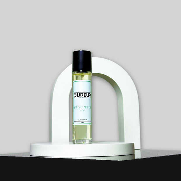 A bottle of perfume labeled 'DUPEUS' placed under a white arch on a grey background, representing the product '006 - Inspired by MFK Gentle Fluidity'.