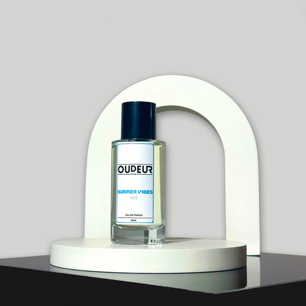 A bottle of perfume displayed on a white stand with a curved top, the liquid is clear and the cap is black. The label reads 'DUPEUR'.
