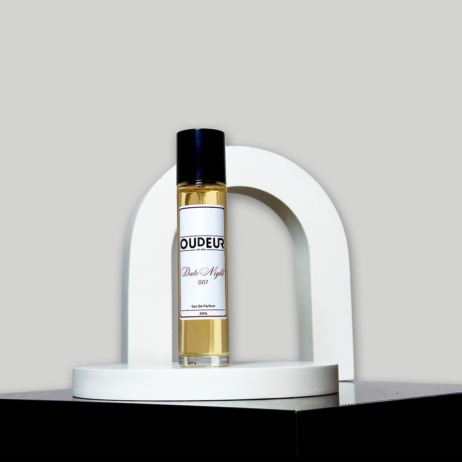 A bottle of perfume with a label that reads 'OUDENA - 007 Inspired by LV Ombre Nomade', placed on a white stand against a neutral background.