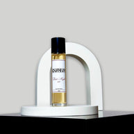 A bottle of perfume with a label that reads 'OUDENA - 007 Inspired by LV Ombre Nomade', placed on a white stand against a neutral background.