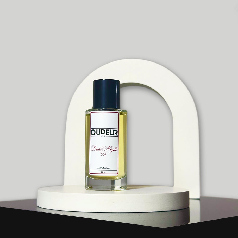 A bottle of perfume with a label that reads 'OUDENA - 007 Inspired by LV Ombre Nomade', placed on a white stand against a neutral background.