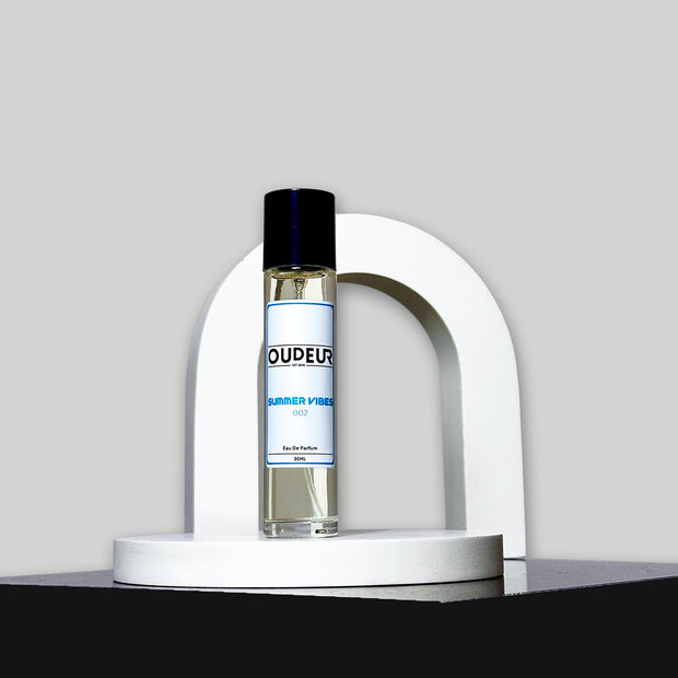 A bottle of 'Inspired by PDM Delina Exclusif' perfume by Parfums de Marly, placed on a white curved stand against a grey background.