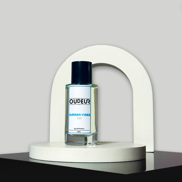 A bottle of 'Inspired by PDM Delina Exclusif' perfume by Parfums de Marly, placed on a white curved stand against a grey background.