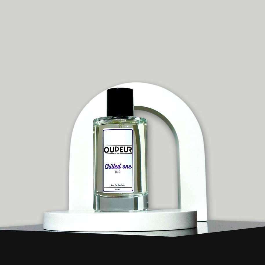 A bottle of unisex fragrance named 'OUDEUR' displayed on a white stand against a neutral background.