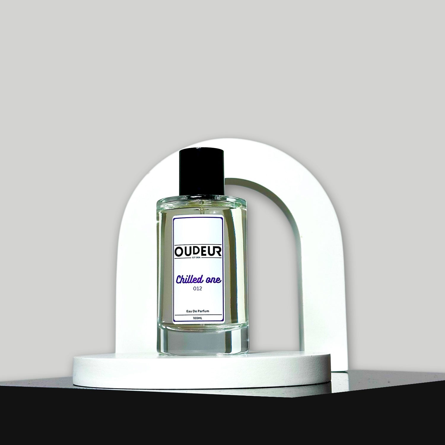 A bottle of unisex fragrance named 'OUDEUR' displayed on a white stand against a neutral background.