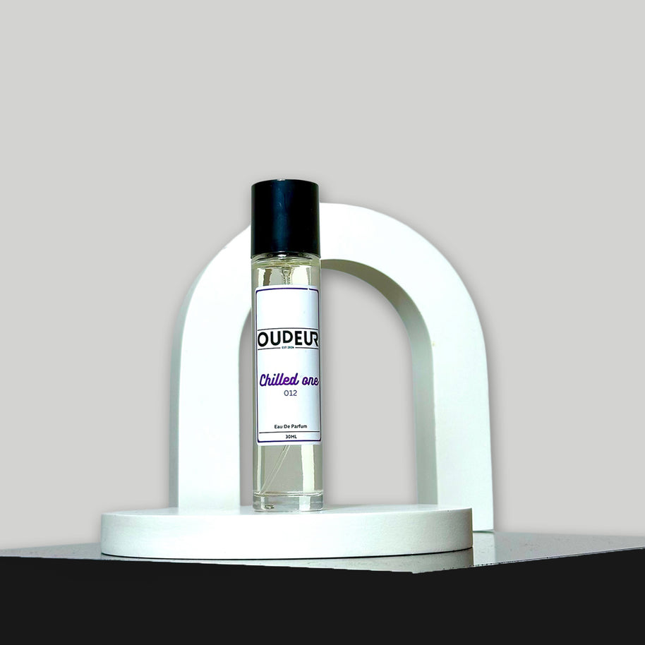 A bottle of unisex fragrance named 'OUDEUR' displayed on a white stand against a neutral background.