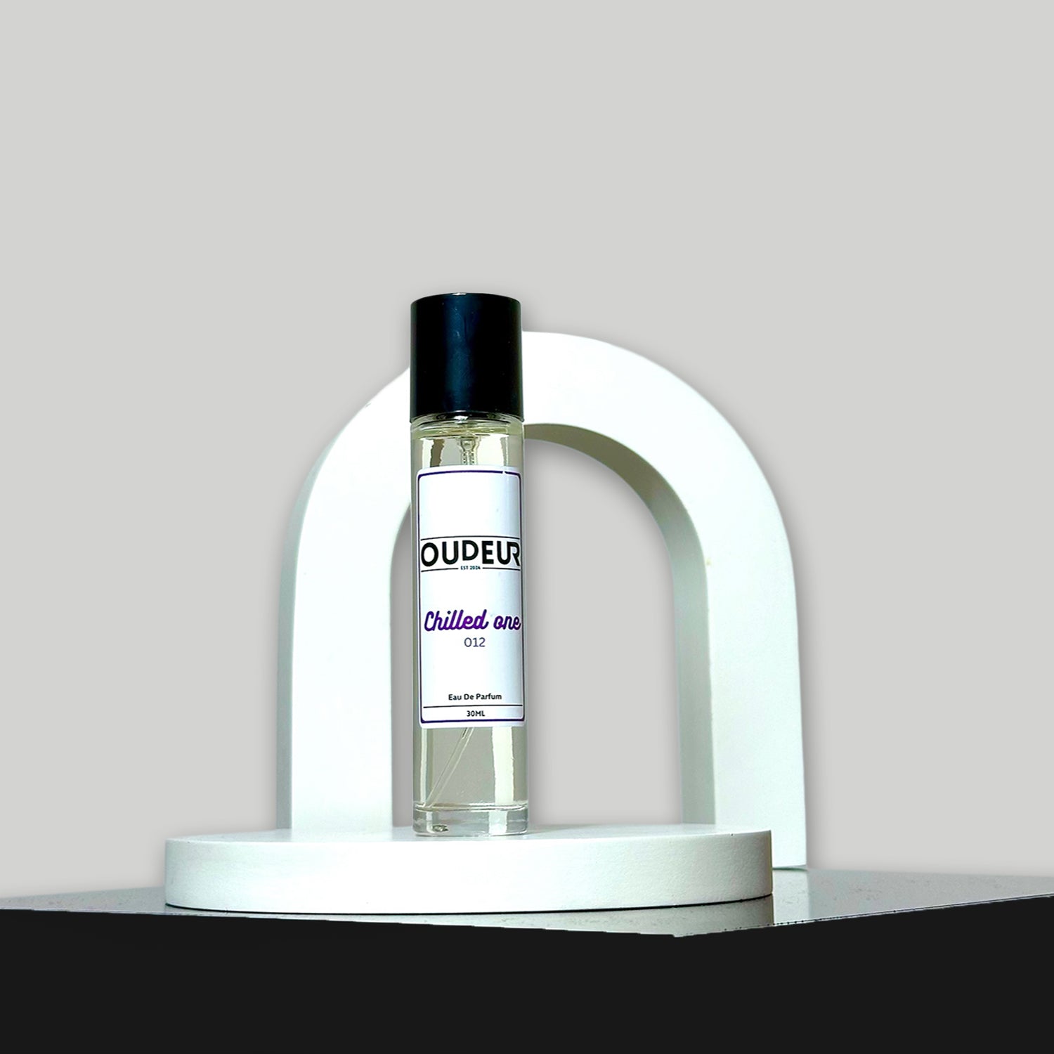 A bottle of unisex fragrance named 'OUDEUR' displayed on a white stand against a neutral background.