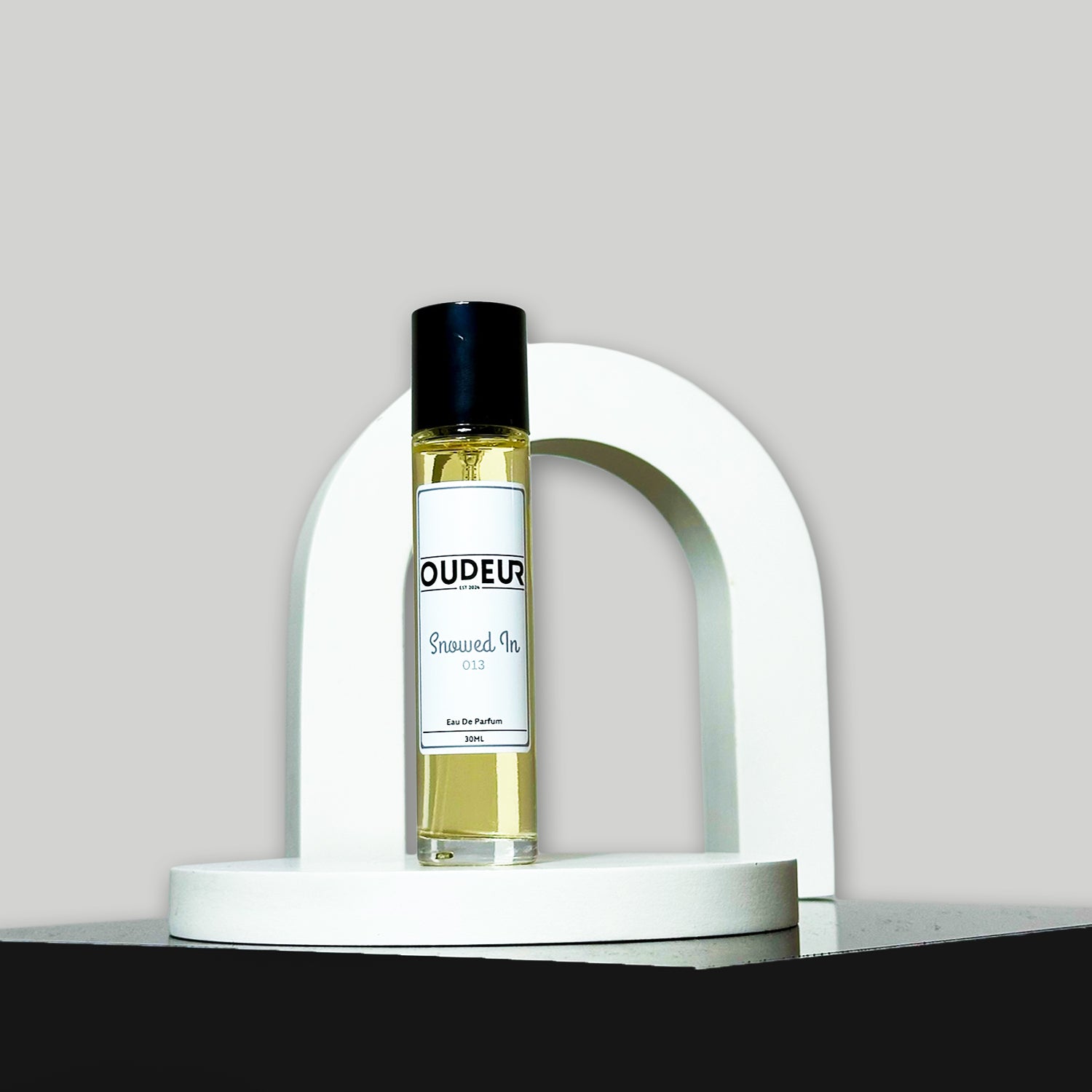 A bottle of perfume with a label that reads 'OUD EAU', placed on a white stand, with a white background.